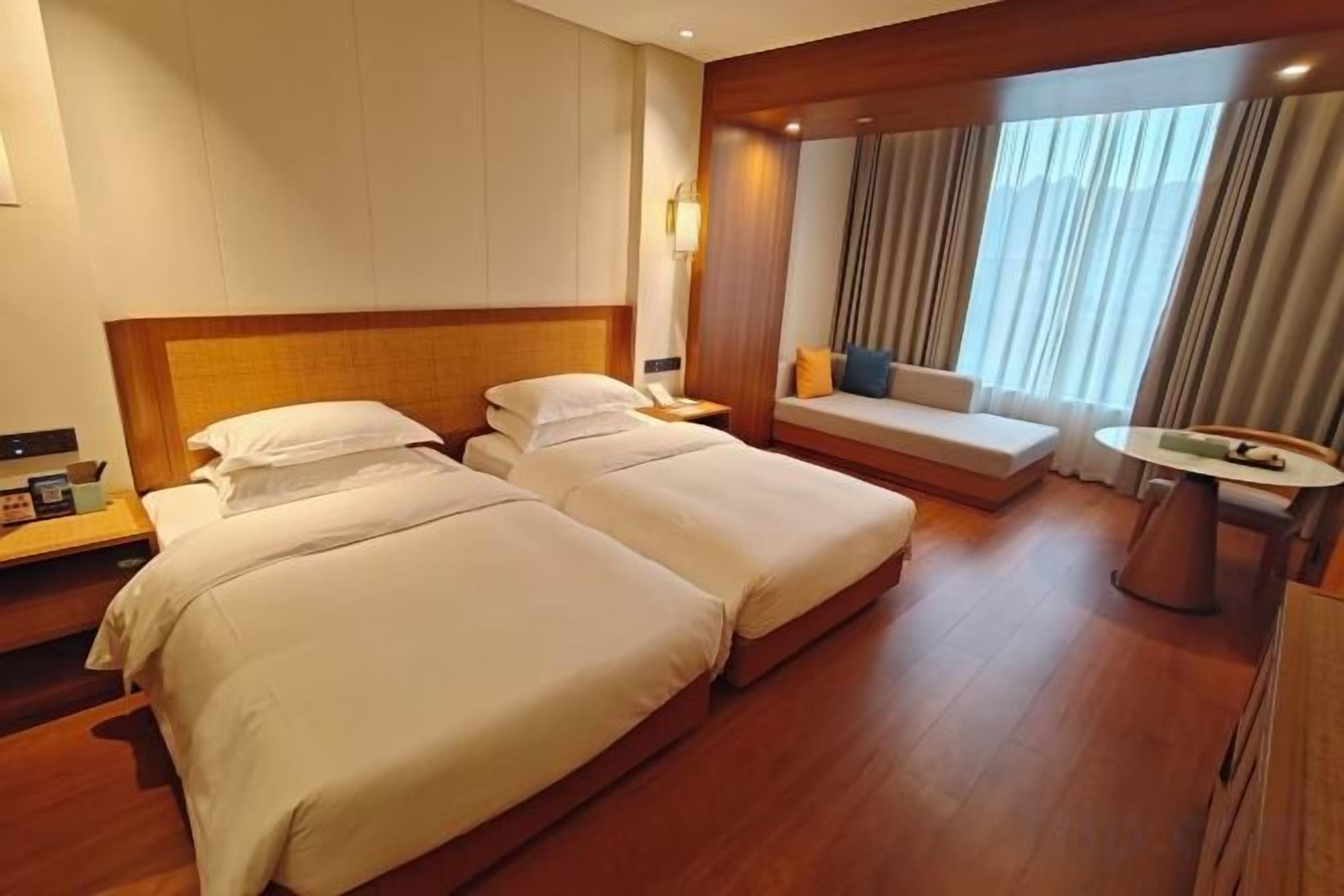 Habitación de hotel con dos camas, un sofá, una mesita y una ventana con cortinas.