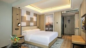 A modern hotel room with a large bed, a desk, a chair, and a small table with a vase of flowers. - Time Platinum (Ziyun)