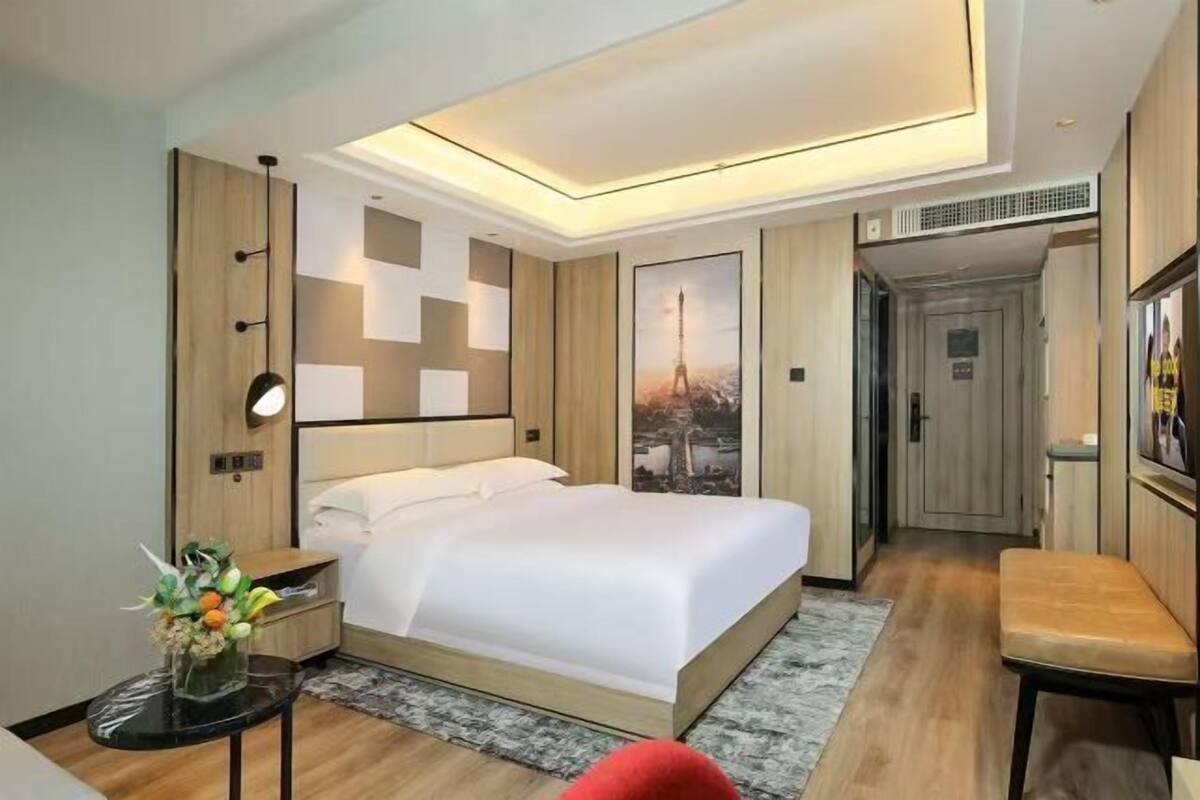 A modern hotel room with a large bed, a desk, a chair, and a small table with a vase of flowers.