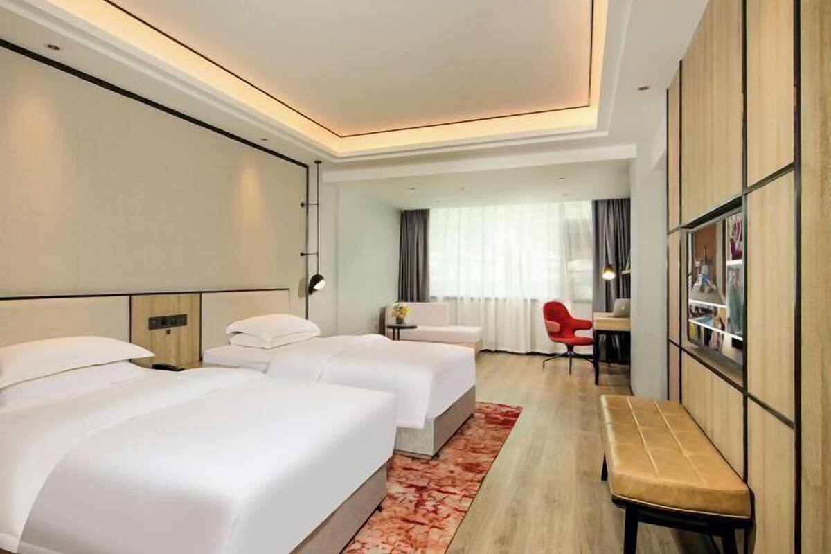 A hotel room with two beds, a desk, a chair, and a bench.