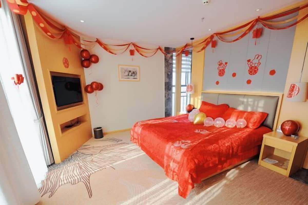 A bedroom with a large bed, a TV, and red decorations.