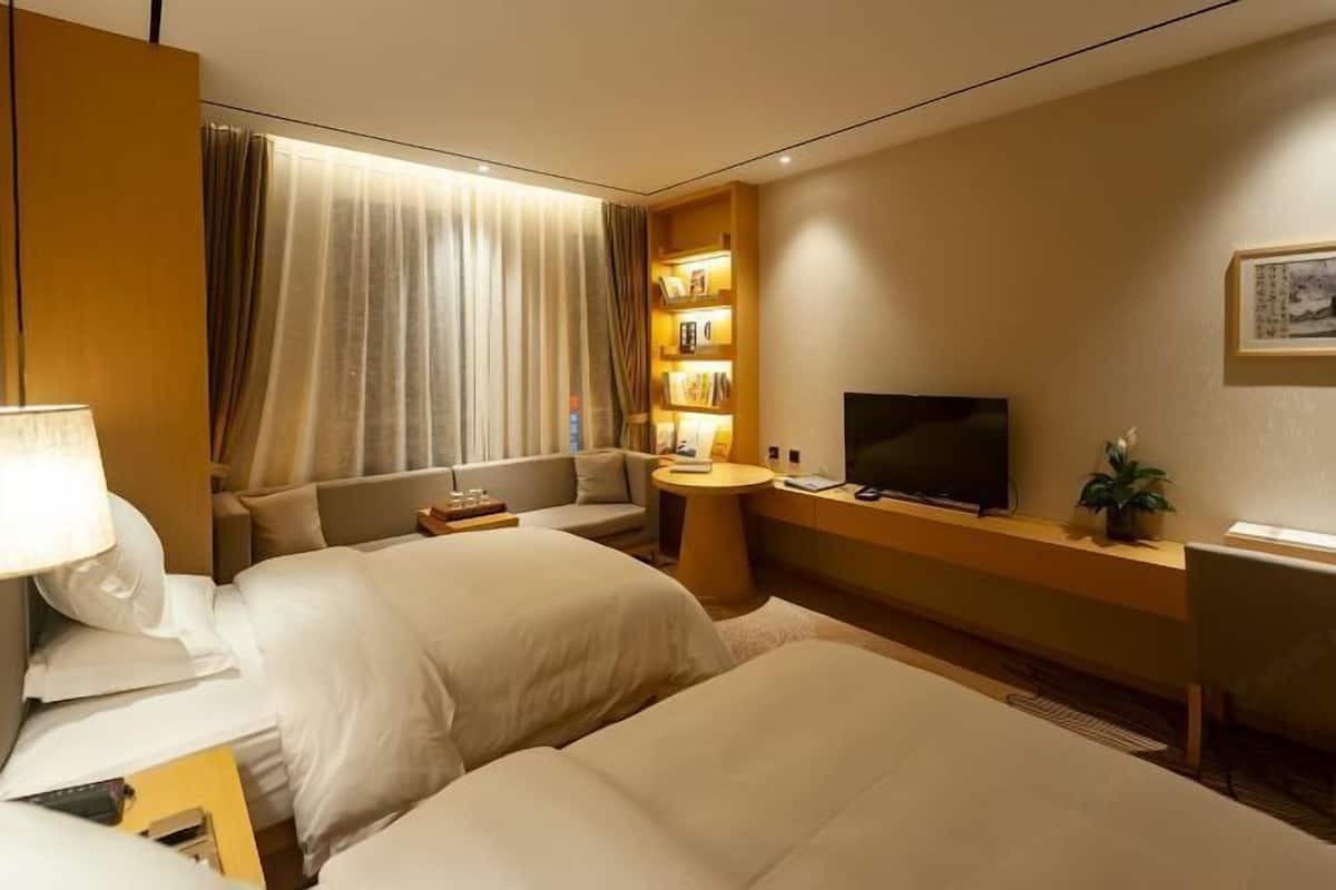 A hotel room with two beds, a sofa, a TV, a small table, and a bookshelf.