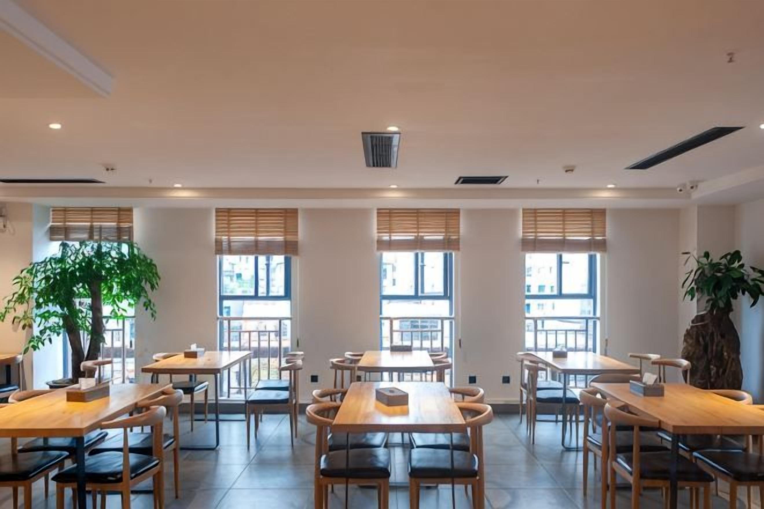 Un amplio comedor interior con varias mesas y sillas, ventanas grandes y una planta central.