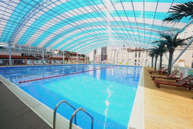 An indoor swimming pool with a glass ceiling, wooden deck, and lounge chairs.