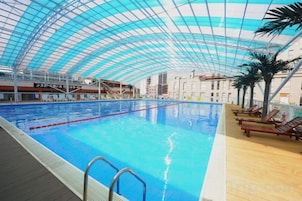 An indoor swimming pool with a glass ceiling, wooden deck, and lounge chairs.