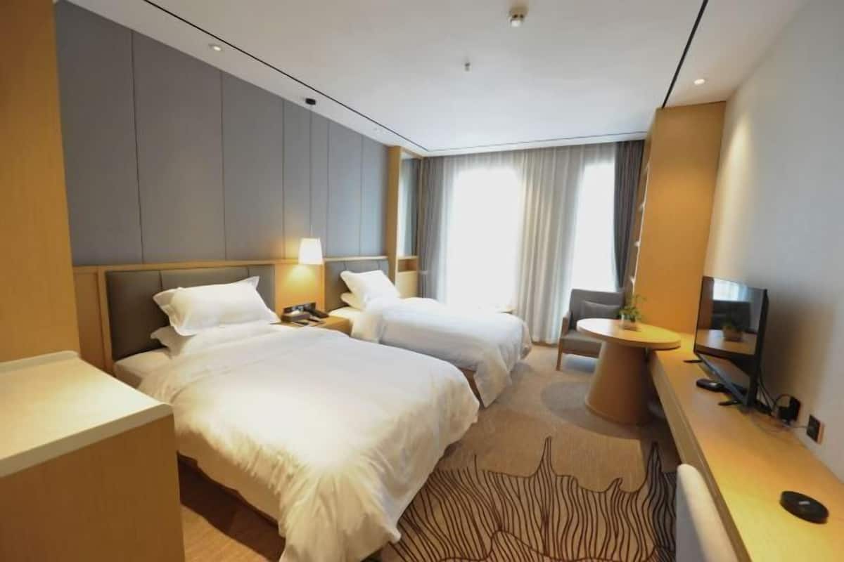 A hotel room with two beds, a desk with a chair, a TV, and a window with curtains.