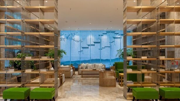 Eine moderne Lobby mit einer zentralen Sitzgelegenheit, Bücherregalen und einem Wandgemälde.