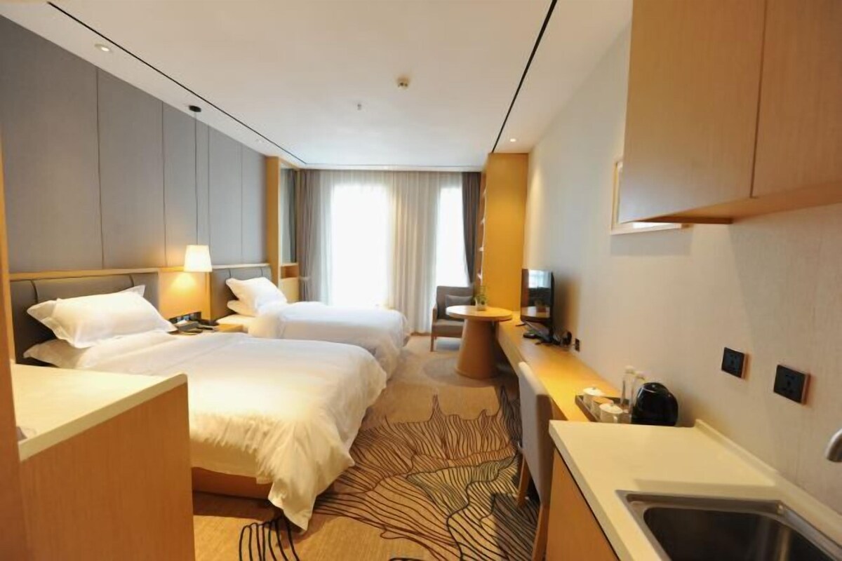 A hotel room with two beds, a desk, a chair, a small table, and a sink.