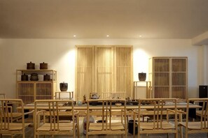 A dining area with a long table, multiple chairs, and a backdrop of bamboo screens. - Deepness Hotel (Qiubei)