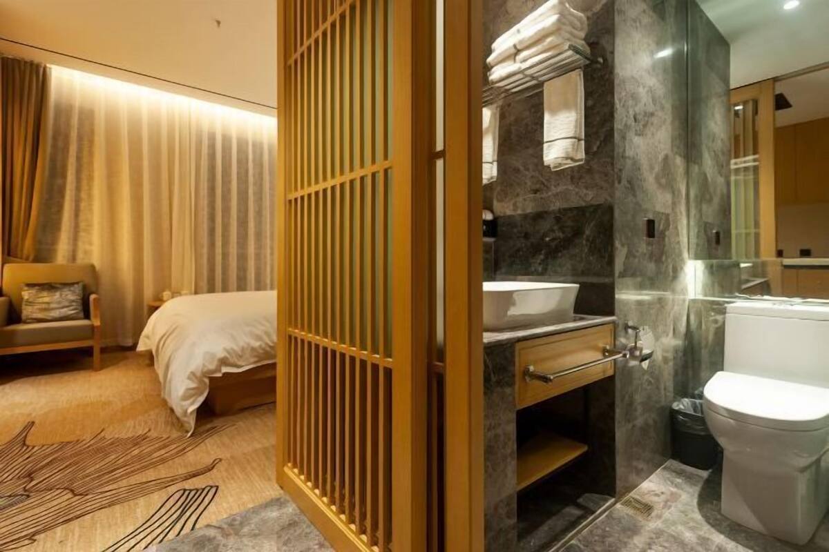 A hotel room with a bed, a bedside table, a bathroom with a sink, mirror, and toilet.