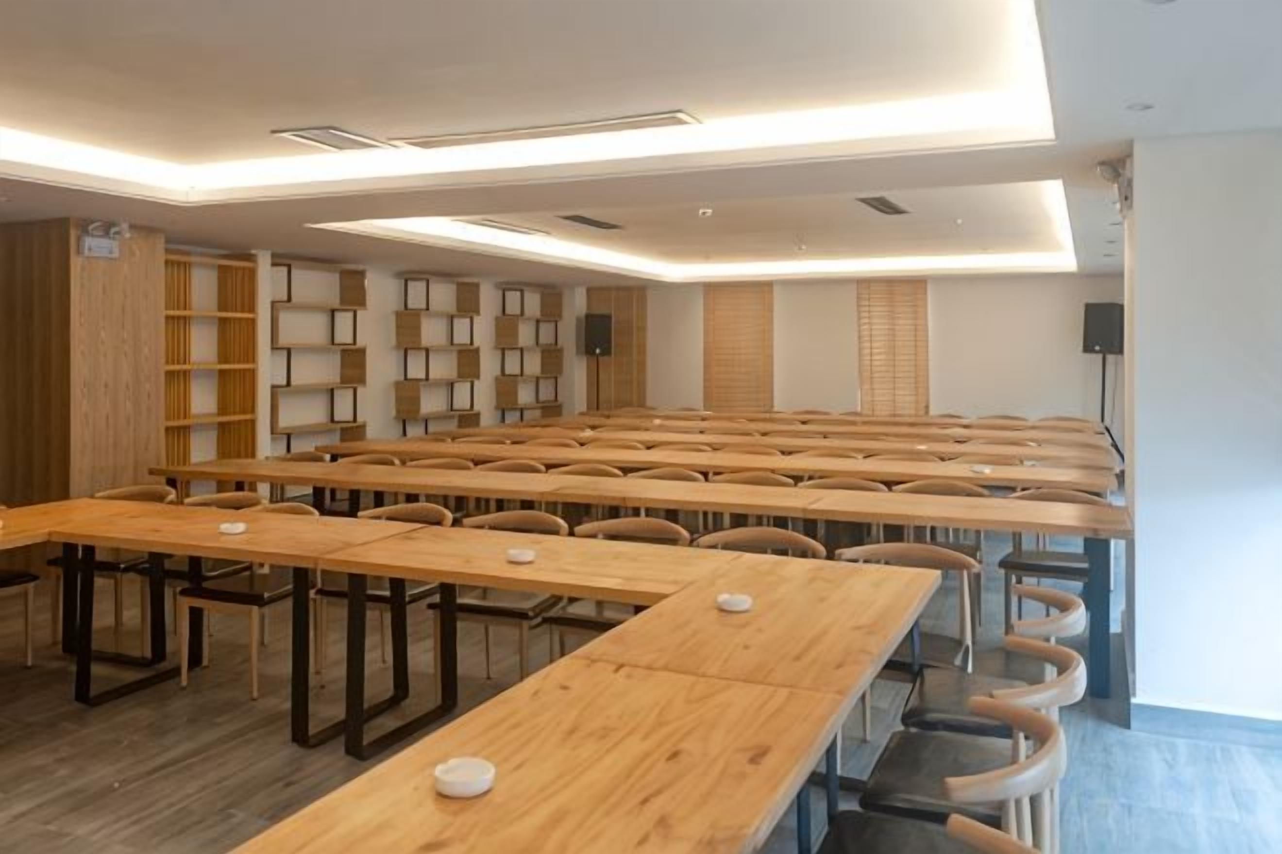 A conference room with multiple wooden tables and chairs, a whiteboard, and a speaker.