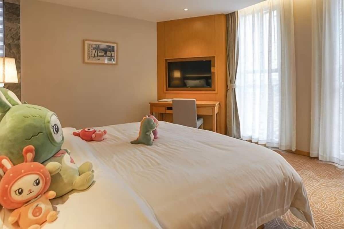 A hotel room with a bed, a desk, a television, and a window with curtains.