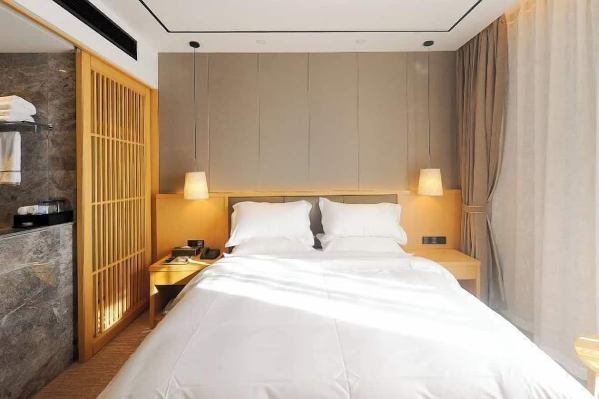 A hotel room with a large bed, two bedside lamps, a wooden wardrobe, and a stone wall.