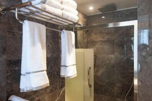 A bathroom with a glass shower door, a towel rack with folded towels, and a marble wall. - Deepness Hotel (Qiubei)