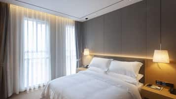 Una habitación de hotel moderna con una cama grande, dos lámparas de noche, una mesita de noche y un ventanal con cortinas translúcidas.