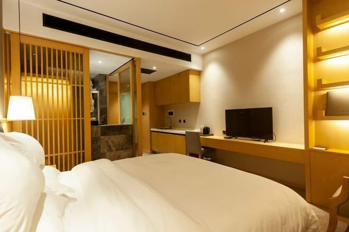 A hotel room with a bed, a desk, a television, and a kitchenette.