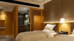 Ein Hotelzimmer mit zwei Betten, einem Nachttisch, einem Schrank und einem Badezimmer, das durch eine offene Tür sichtbar ist.