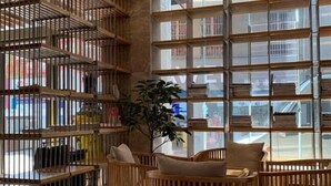 Ein Zimmer mit großem Fenster, einer Bücherwand und einer Sitzecke mit Pflanze.