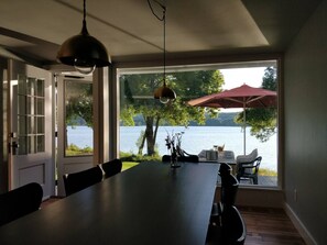 A dining area with a large table, chairs, and a view of a lake through a large window.