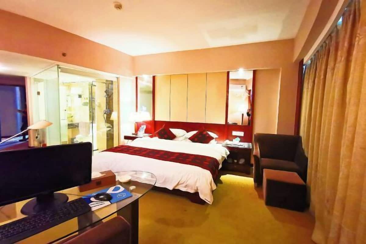 A hotel room with a bed, a desk with a computer, a chair, and a bedside table.