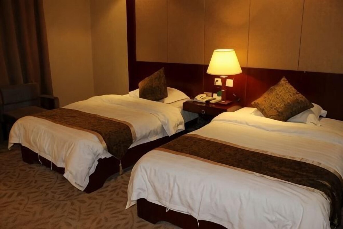 Two single beds with headboards, a bedside table with a lamp, and a chair in a hotel room.