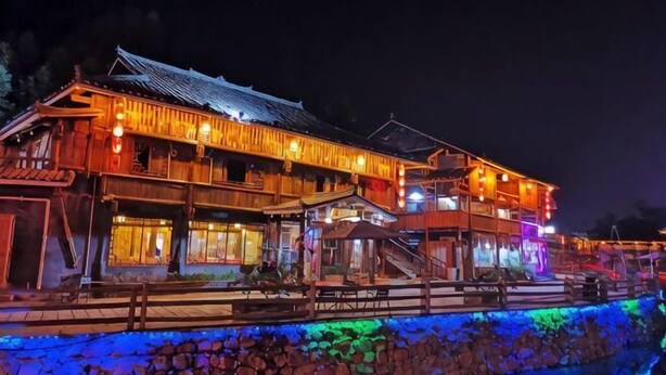 A traditional wooden building with a sloped roof, a wooden deck, and a stone wall. - Rongshui Miaoshan International Hotel (Rongshui)