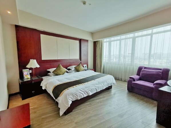 A hotel room with a large bed, a desk with a lamp, a purple armchair, and a view through the window. - Rongshui Miaoshan International Hotel (Liuzhou)