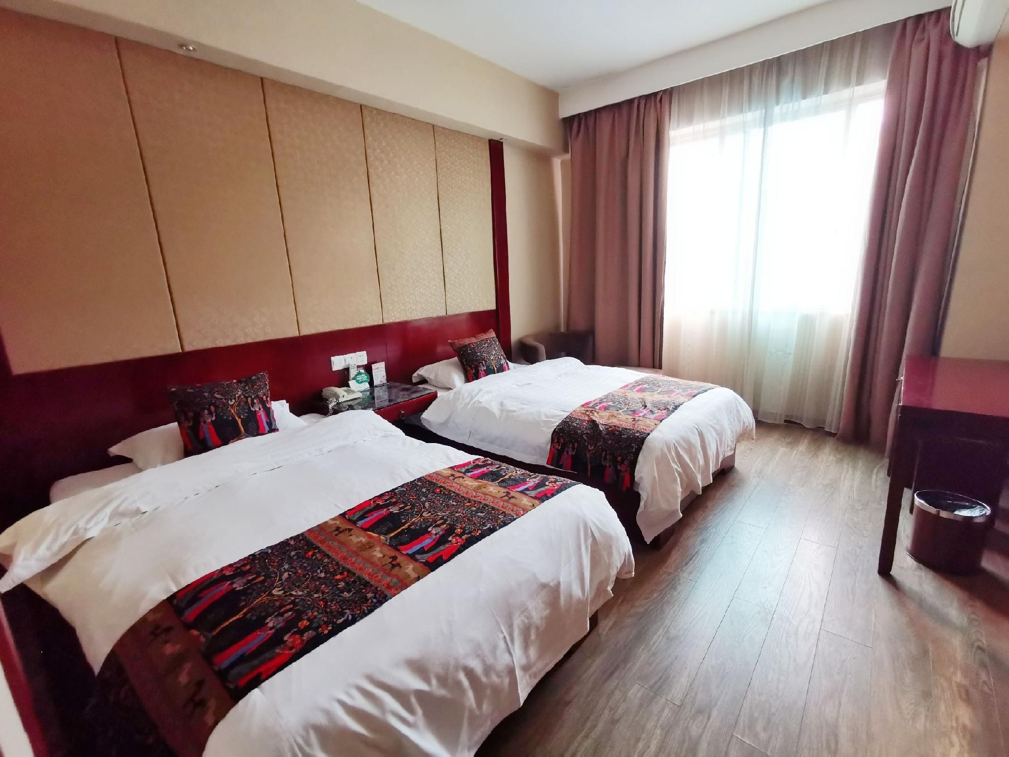Hotellihuone, jossa on kaksi sänkyä, puulattia, suuri ikkuna, jossa on verhot, ja seinälle asennettu televisio.