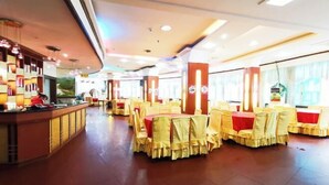 A restaurant with round tables covered in yellow tablecloths and chairs, a counter with a person behind it, and large windows allowing natural light. - Rongshui Miaoshan International Hotel (Rongshui)