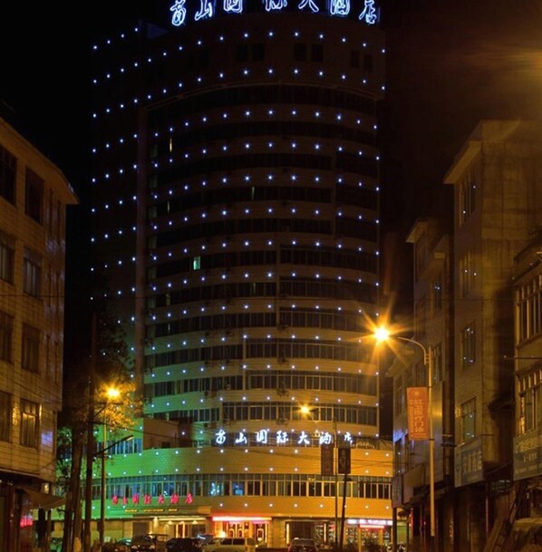 Un hotel de varios pisos con fachada curva, ventanas iluminadas y un letrero llamativo en la parte superior.