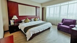 A hotel room with a large bed, a nightstand, a purple armchair, and a view of the city through large windows. - Rongshui Miaoshan International Hotel (Liuzhou)