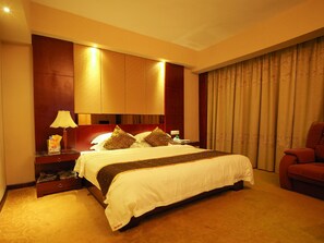 A hotel room with a large bed, a nightstand, a lamp, a red armchair, and a window with curtains. - Rongshui Miaoshan International Hotel (Liuzhou)