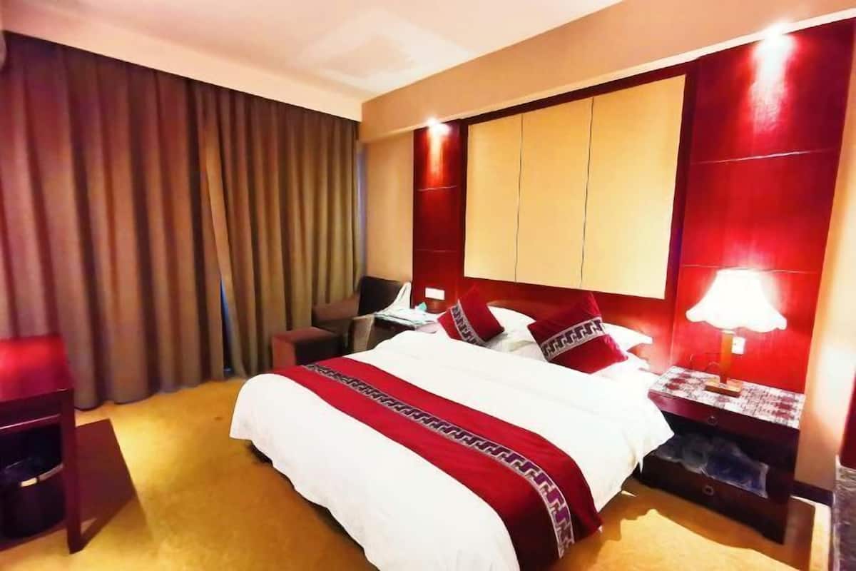 A hotel room with a large bed, a desk, a chair, and a nightstand with a lamp.