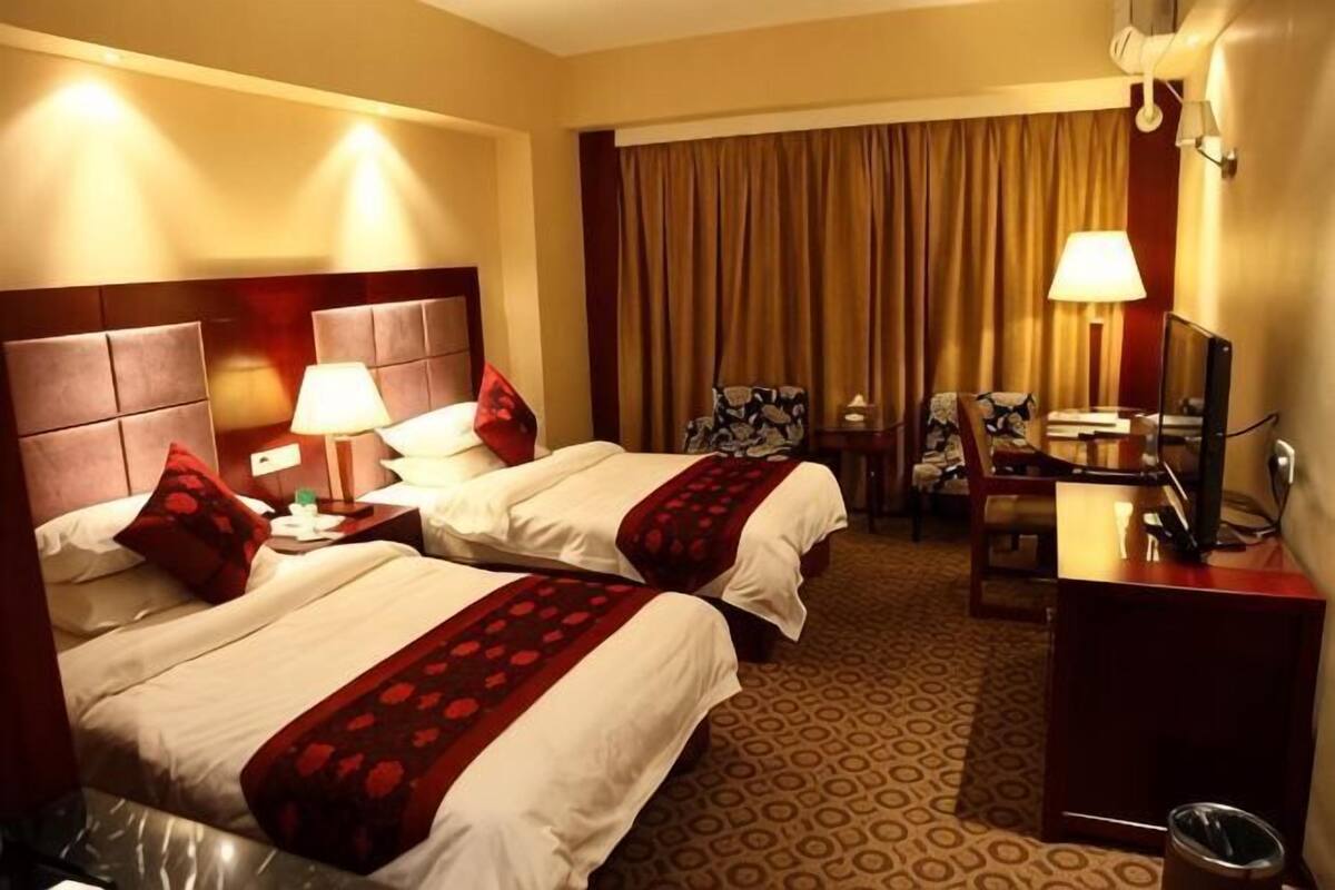A hotel room with two beds, a desk, a chair, a TV, and a window with curtains.