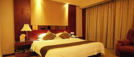 A hotel room with a large bed, a nightstand with a lamp, a red chair, and a window with curtains.