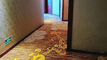 Corredor de hotel com carpete estampado e luminária fixada na parede.