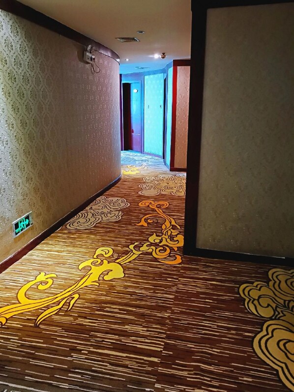 A hotel hallway with patterned carpet and a wall-mounted light fixture.