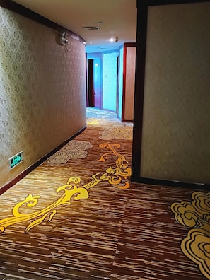 Pasillo de hotel con alfombra estampada y una lámpara fijada a la pared.