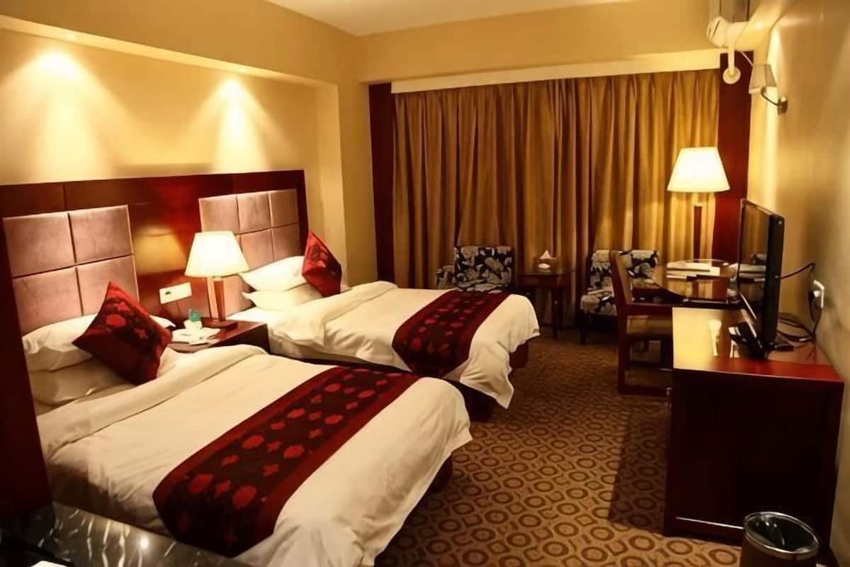 A hotel room with two beds, a desk, a chair, a television, and a window with curtains.