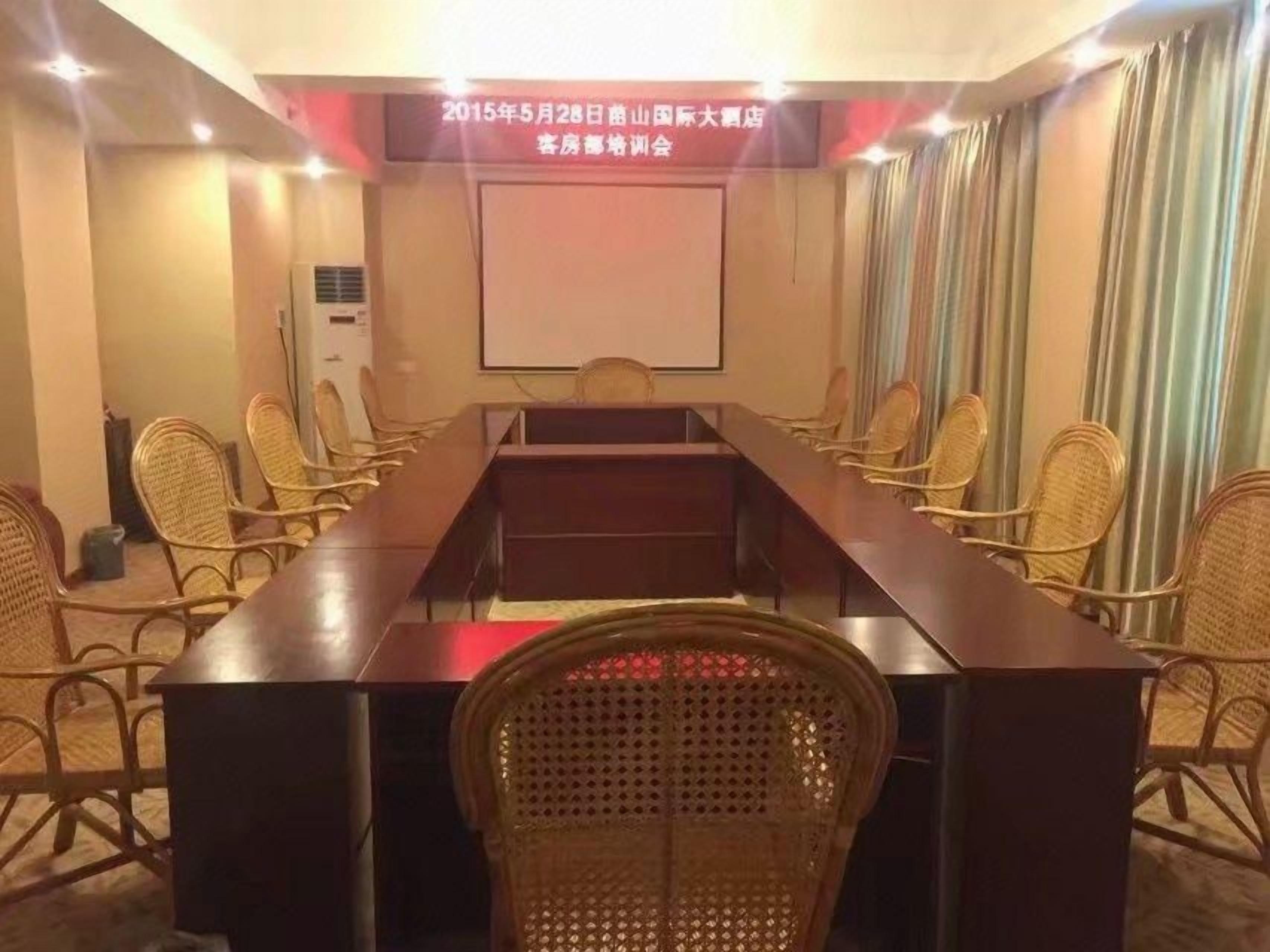 Una sala de conferències amb una taula llarga, cadires, una pantalla de projector i un aire condicionat fixat a la paret.