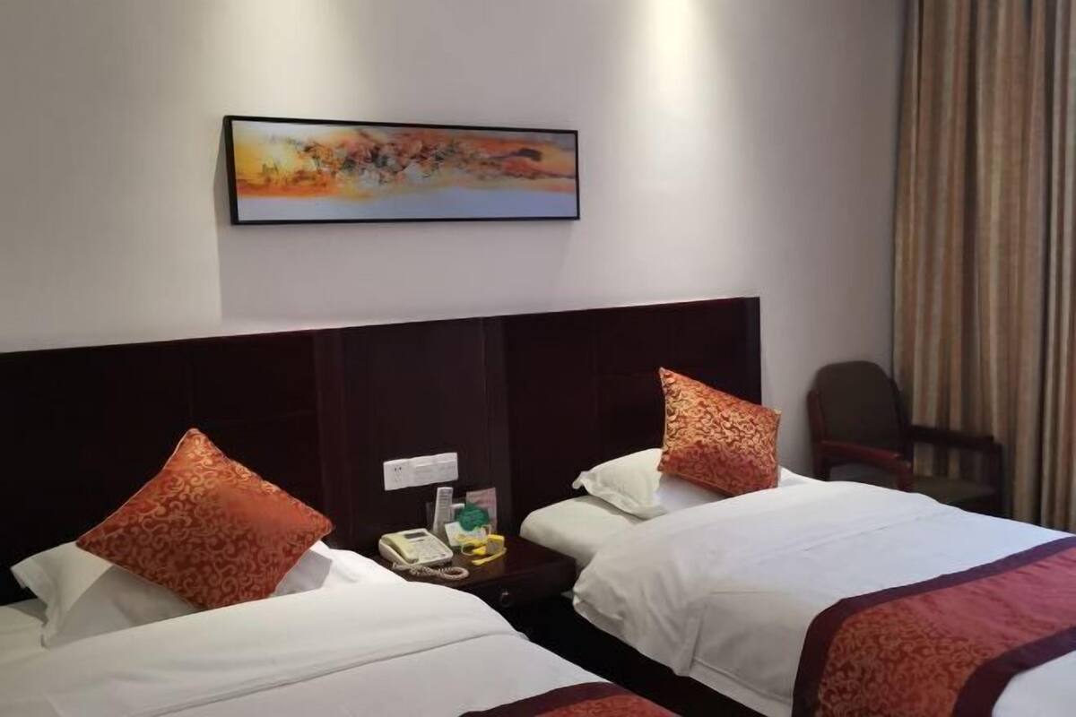 A hotel room with two beds, a headboard, a nightstand with a phone, a painting on the wall, and a chair.
