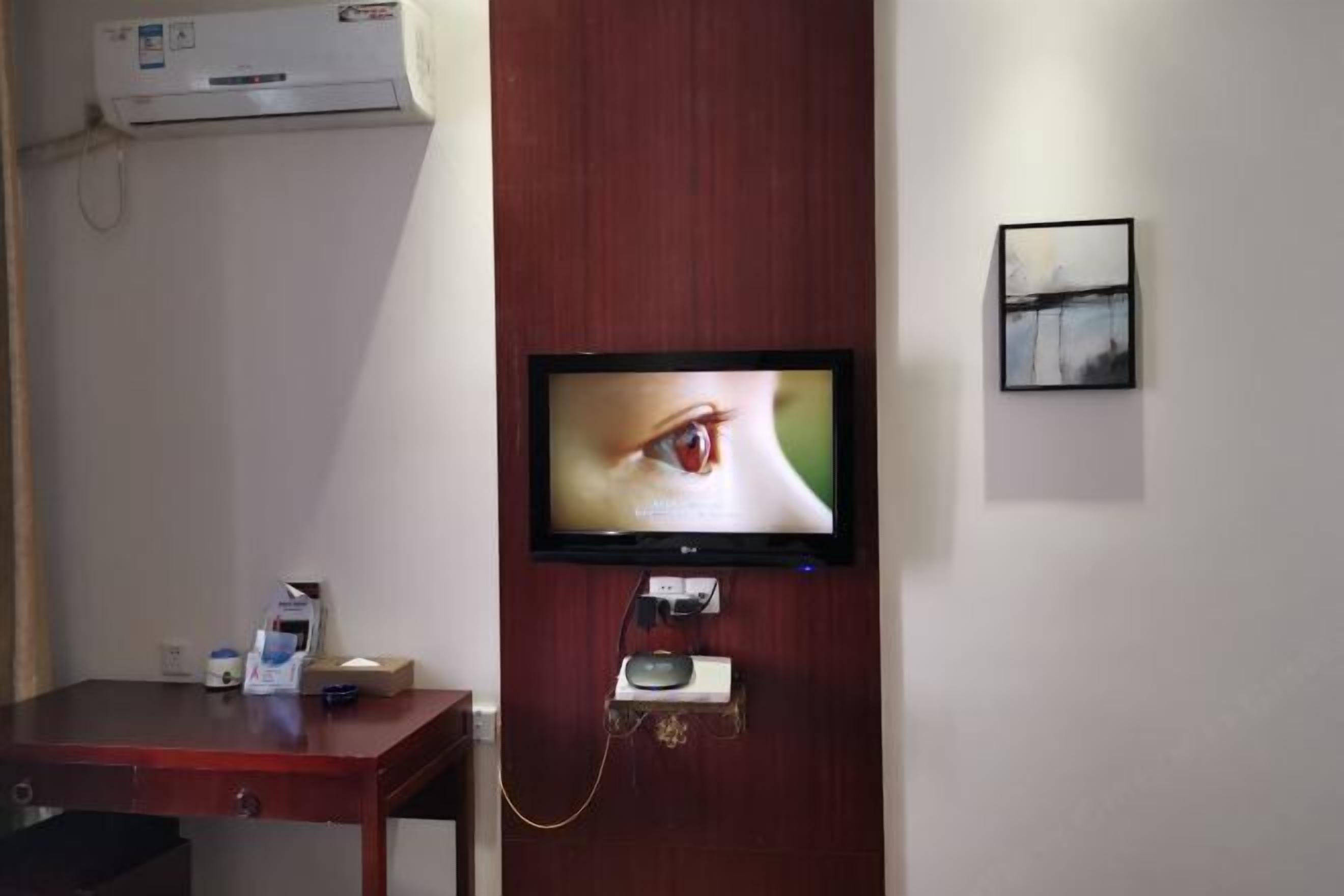 A television mounted on a wooden wall, a small table with a remote control, and a framed picture.
