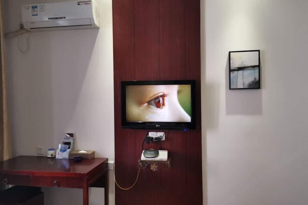 A television mounted on a wooden wall, a small table with a remote control, and a framed picture.