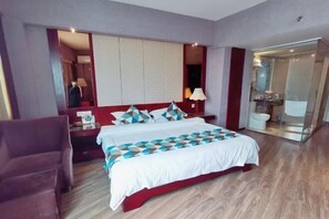 A hotel room with a large bed, a red accent wall, a nightstand, a lamp, and a bathroom visible through a glass door. - Rongshui Miaoshan International Hotel (Liuzhou)