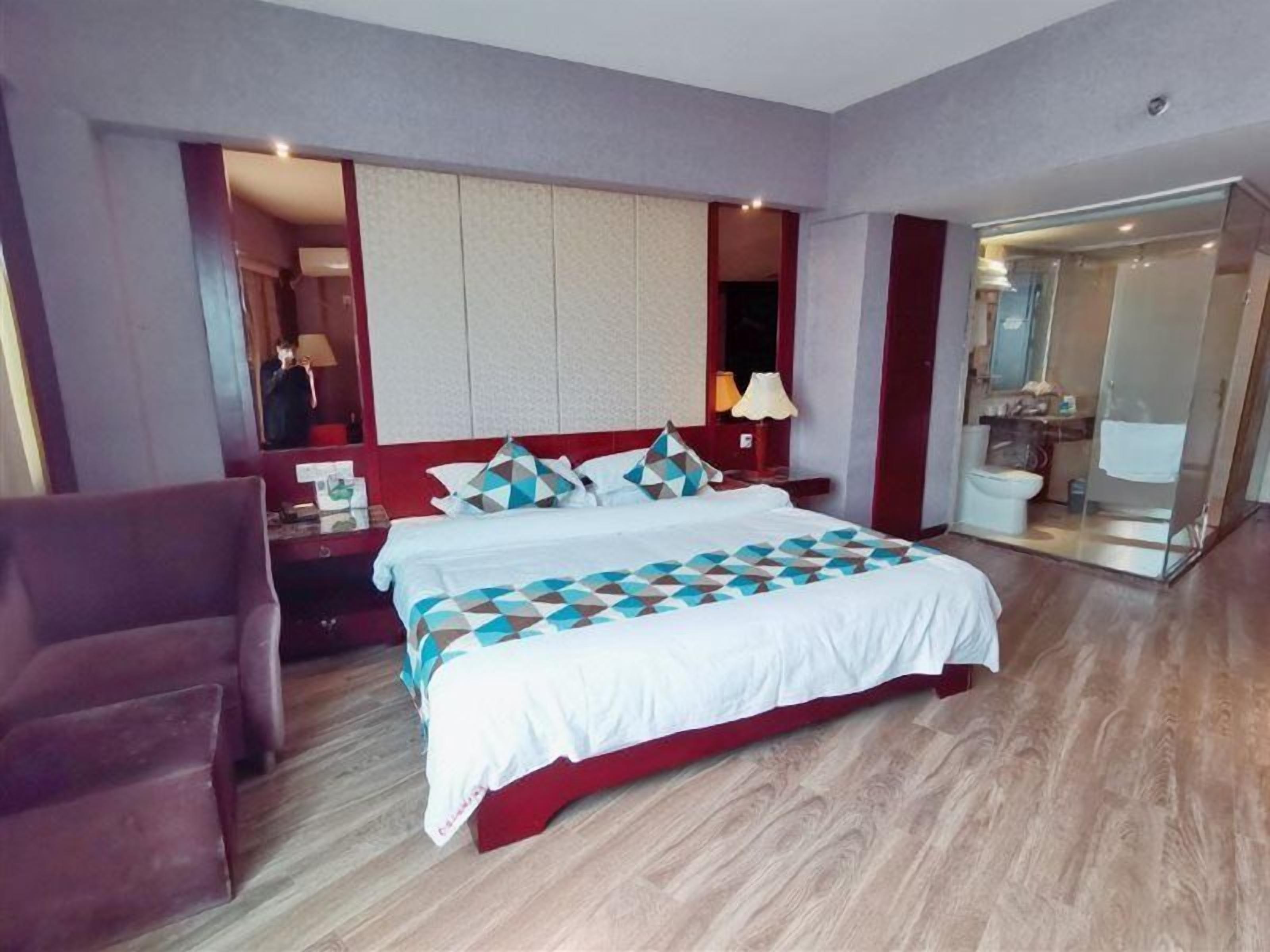 Ein Hotelzimmer mit Bett, Stuhl, Nachttisch, Spiegel und angrenzendem Badezimmer.