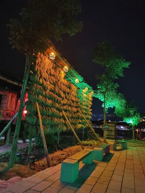 A nighttime outdoor area with a structure covered in foliage, illuminated by warm and green lights, and a paved walkway with benches. - Rongshui Miaoshan International Hotel (Liuzhou)