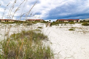 A sandy beach with a pathway leading to a row of red-roofed buildings. - Ocean and Racquet 8110 (St. Augustine)