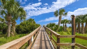A wooden boardwalk leading through a tropical landscape with palm trees and a clear sky. - Ocean and Racquet 8110 (St. Augustine)