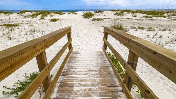 A wooden boardwalk leading to a beach with sand dunes and sparse vegetation. - Ocean and Racquet 8110 (St. Augustine)