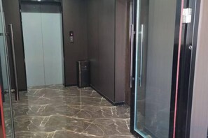 Een lift met marmeren vloer, een prullenbak en een deur met een rode streep.